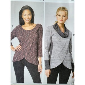 Könnte beinhalten: Zwei Frauen präsentieren Oberteile. Das erste Oberteil ist ein Wickelstil mit einem rosa-schwarzen Zickzackmuster. Das zweite Oberteil ist grau mit einem Wasserfallkragen und dunkelgrauen Seitenteilen und Manschetten. Beide Frauen tragen schwarze Leggings.