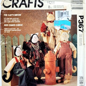 Op de afbeelding: Een McCall's Crafts naaipatroon-envelop P3667 getiteld The Cat's Meow met illustraties van vier stoffen kattenpoppen in verschillende outfits, waaronder een rood geruite jurk, een bloemenjurk en een tuinbroek, staand bij een rode brandkraan.