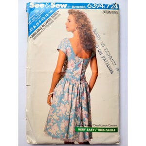 May include: A See & Sew by Butterick 6394 sewing pattern envelope featuring a light blue dress with a pink and white floral print. The dress has short sleeves, a scoop back, and a button-down back closure. The envelope includes size information.
