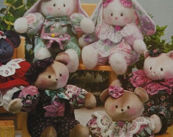 May include: A collection of handmade plush toys, including bunnies and bears. The toys are dressed in floral patterned fabrics and lace, with soft pastel colors. Some have hats and bows, creating a whimsical and vintage aesthetic.