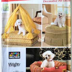May include: A Simplicity pattern for decorative pet beds. The image shows three different pet bed designs, including a canopy bed, an ottoman-style bed, and a round bed with a ruffled edge. The beds are shown with small white dogs.