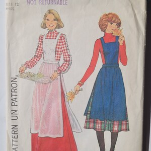 May include: Simplicity sewing pattern number 8114 for a dress with an apron overlay. The pattern is for size 12 and is not returnable. The pattern shows two models wearing the dress, one in a red and white plaid shirt and a white apron, and the other in a red turtleneck and a blue denim apron.
