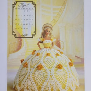 May include: A 1992 calendar showing a doll in a yellow and white crocheted dress with floral details. The calendar displays the month of April. The doll has blonde hair and is set against a yellow and white backdrop.