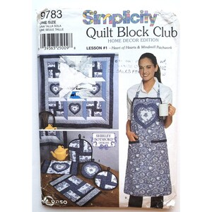 May include: Simplicity Quilt Block Club Home Decor Edition pattern. The image shows a woman wearing an apron with a heart design, and a quilt with heart and windmill patterns. The pattern includes instructions for various home decor items.
