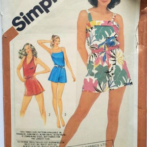 Puede incluir: Un sobre de patrón de costura Simplicity con ilustraciones de tres estilos de monos cortos. Uno tiene un estampado de hojas tropicales en verde, rosa y blanco, mientras que los otros son de color rojo y azul sólido. El sobre incluye texto y tallas.