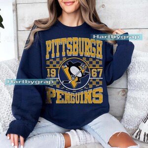 Pu&ograve; includere: Felpa blu navy con il logo dei Pittsburgh Penguins in oro e bianco. Il logo include un pinguino che gioca a hockey, l'anno 1967 e il nome della citt&agrave;. Girocollo e maniche lunghe.
