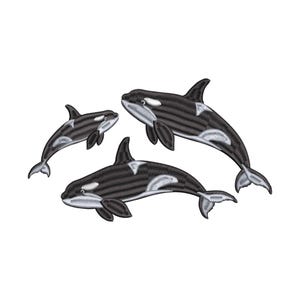 Puede incluir: Diseño bordado con tres orcas en blanco y negro. Las orcas se representan nadando, con puntadas detalladas que crean una apariencia texturizada. El diseño está sobre un fondo blanco liso.