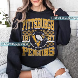 Pu&ograve; includere: Felpa nera con grafica vintage del logo dei Pittsburgh Penguins e la scritta "PITTSBURGH PENGUINS 1967". Il logo presenta un pinguino in uniforme da hockey. Il testo e il logo sono in oro e bianco.