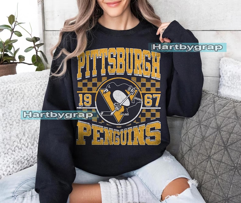 Pu&ograve; includere: Felpa nera con grafica vintage del logo dei Pittsburgh Penguins e la scritta "PITTSBURGH PENGUINS 1967". Il logo presenta un pinguino in uniforme da hockey. Il testo e il logo sono in oro e bianco.