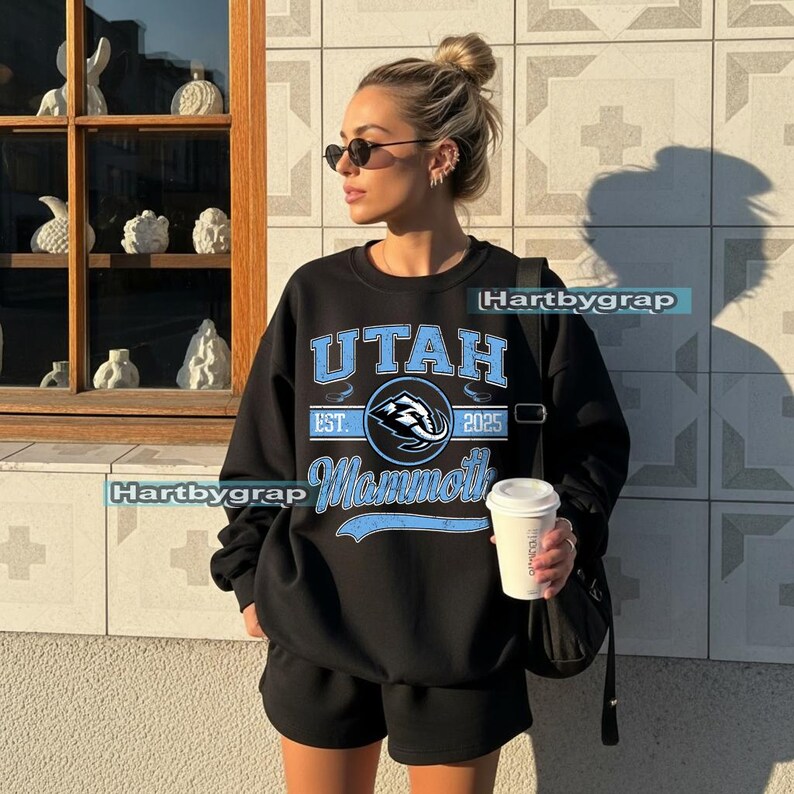 May include: Black sweatshirt with the text "UTAH Mammoth" in light blue. The sweatshirt has a crew neck and is paired with black shorts. The image also includes a coffee cup and sunglasses.