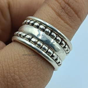Può includere: Un anello d'argento con più fasce, caratterizzato da una combinazione di texture lisce e perline. L'anello è indossato su un dito, mostrando il suo design a strati e la finitura lucida. Il testo "925Silvergems2026" è visibile sull'anello.