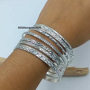 Puede incluir: Un conjunto de pulseras de plata con intrincados diseños florales y de hojas. Las pulseras se apilan en una muñeca, mostrando los diseños detallados y la calidad brillante y reflectante del metal. El texto "925Silvergems2026" es visible.