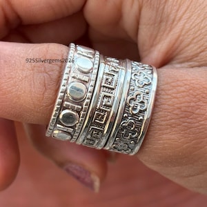 Puede incluir: Primer plano de varios anillos de plata con diseños intrincados. Los anillos presentan patrones de círculos, formas geométricas y motivos florales. Los anillos están apilados en un dedo, mostrando la artesanía detallada. El texto "925silvergems2026" es visible.