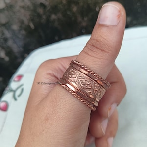 May include: Copper-colored ring set on a finger. The rings have various designs, including a braided texture and a geometric pattern. The text "925silvergems2026" is visible. The rings are stacked together, creating a layered effect.