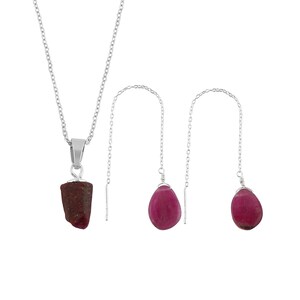 May include: A silver necklace with a dark red, rough-cut pendant and a pair of silver threader earrings with teardrop-shaped, deep pink gemstones. The jewelry set is displayed against a white background.