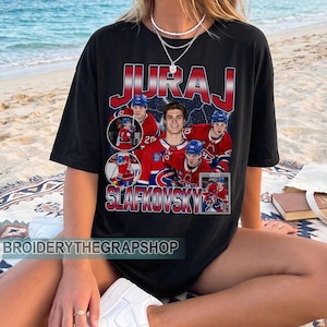 Könnte beinhalten: Ein schwarzes T-Shirt mit kurzen Ärmeln und einem Grafikdruck des Eishockeyspielers Juraj Slafkovsky. Das Design zeigt mehrere Action-Aufnahmen des Spielers im roten Trikot, den Namen JURAJ SLAFKOVSKY in fetten roten und blauen Buchstaben sowie eine Signatur.