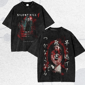 May include: Dark gray t-shirt with a distressed graphic design. The front features the text "SILENT HILL f" and an illustration of a person. The back has Japanese text and a face graphic.