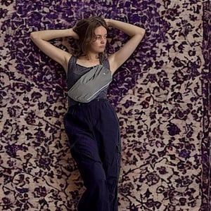Puede incluir: Una camiseta sin mangas de color gris oscuro combinada con pantalones cargo de color azul marino holgados y un bolso cruzado de color gris claro con una franja horizontal reflectante en la parte delantera, cruzado sobre el pecho.