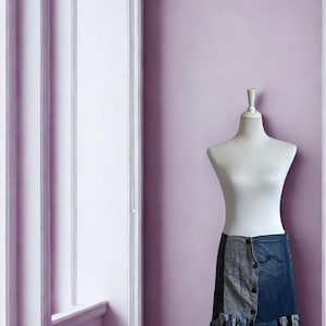 Könnte beinhalten: Ein Jeansrock mit Patchwork-Design und Knopfverschluss wird auf einer weißen Schneiderpuppe präsentiert. Der Rock hat eine Mischung aus blauen und grauen Jeans-Einsätzen mit einem Fransen-Saum. Der Hintergrund ist eine hellviolette Wand.