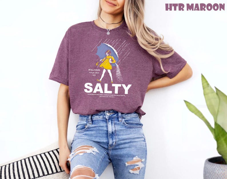 Op de afbeelding: Bordeauxrood t-shirt met een afbeelding van een persoon onder een paraplu, met het woord "SALTY" in het wit. De afbeelding bevat ook de tekst "All the flavors and you chose to be..."