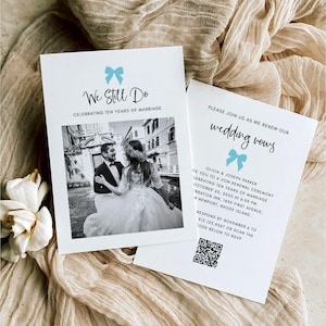 May include: Two white wedding vow renewal cards with light blue bow accents. One card reads "We Still Do" and features a black and white photo of a couple. The other card says "wedding vows" and includes event details.