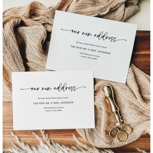 May include: Two white cards with the text "our new address" in elegant script. The cards also include the text "We have moved! Please keep in touch" and the new address of "THE NEW MR. & MRS. ANDERSON". A gold wax seal and stamp are also visible.