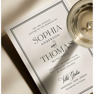 Op de afbeelding: Een crèmekleurige trouwkaart met zwarte tekst en een dubbele lijnrand. De tekst luidt: You are joyfully invited to the wedding of Sophia Anderson and Thomas Mitchell, Saturday, September ninth, two thousand twenty-eight, at seven o'clock, Villa Giulia, Madison, New Jersey, reception to follow.