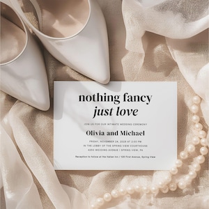 May include: A wedding invitation with the text "nothing fancy just love" and details for Olivia and Michael's ceremony. The invitation is next to a pair of white heels and a string of pearls on a beige fabric.