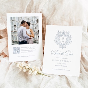 以下が含まれることがあります： 2 つの白い結婚式の招待状。1 つのカードには、カップルの写真、QR コード、ウェブサイトのアドレスが掲載されています。もう一方のカードには、カップルの名前、結婚式の日付、場所とともに「Save the Date」と書かれています。花の模様も付いています。