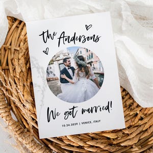 Könnte beinhalten: Eine weiße Hochzeitsankündigungskarte mit einem Foto eines Paares in Venedig, Italien. Die Karte zeigt den Text "The Andersons" und "We got married!" mit dem Datum 10.24.2029. Die Karte liegt auf einer geflochtenen Korbweide.