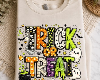 May include: A beige crewneck sweatshirt featuring the text TRICK OR TREAT in large, multi-patterned letters. The design includes skulls, candy corn, spiderwebs, bats, ghosts, a black cauldron with green liquid, and small stars in orange and green.