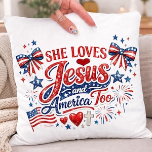 Könnte beinhalten: Ein weißes quadratisches Dekokissen mit einem patriotischen Aufdruck und dem Text SHE LOVES Jesus and America Too. Das Design zeigt rote und blaue Schleifen, Sterne, Feuerwerk, eine kleine amerikanische Flagge, zwei rote Herzen und ein silbernes Kreuz.