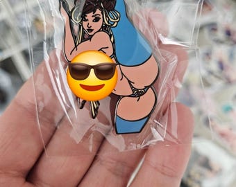 May include: A pin featuring a cartoon illustration of a woman in a blue outfit. The pin is in a clear plastic package. The woman has dark hair and is in a dynamic pose. The pin has a gold border.