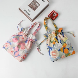 May include: Two floral drawstring bags with matching handles. One bag features pink, blue, and white flowers, while the other has yellow, blue, and orange flowers. The bags are made of a soft fabric and have a gathered top.