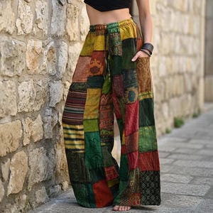 May include: Wide-leg pants featuring a patchwork design with various rectangular fabric panels in shades of green, yellow, red, and brown. The pants have an elasticized waistband with a drawstring and side pockets, showcasing diverse geometric patterns.
