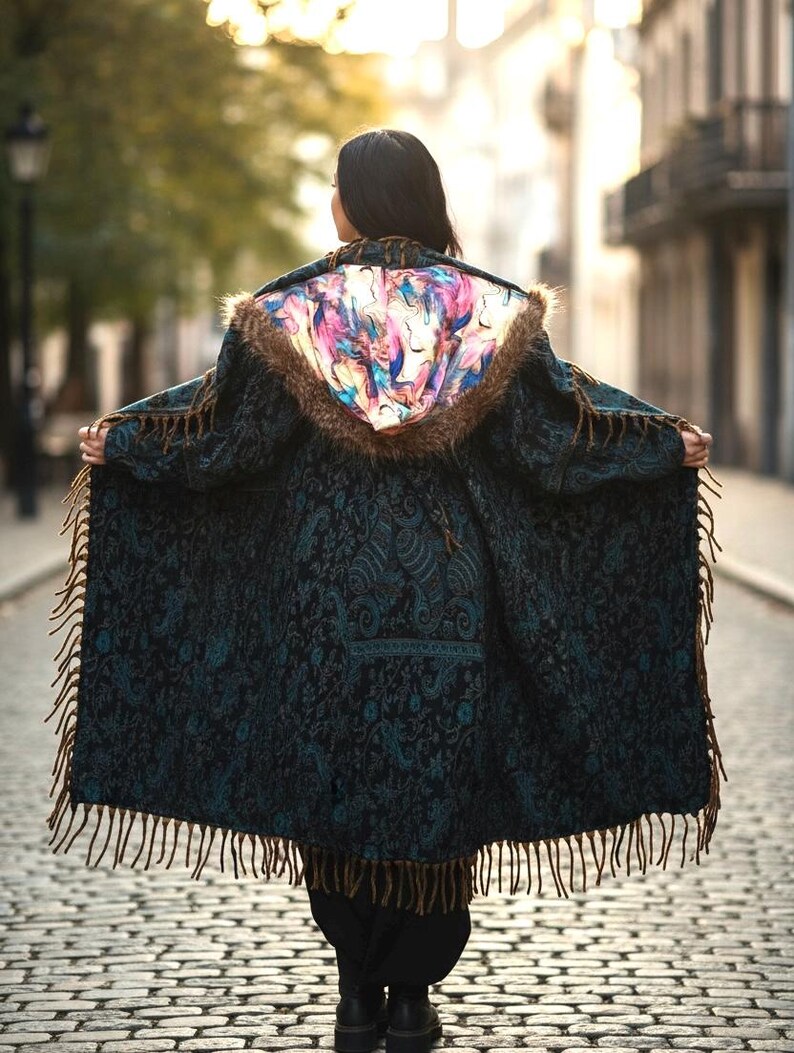 May include: A dark teal coat with a paisley pattern and brown fringe. The hood features a colorful abstract design and faux fur trim. The coat is open, revealing the back of a person walking on a cobblestone street.