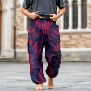 May include: Loose-fitting trousers featuring a tie-dye pattern in shades of deep red and dark blue. The pants have an elasticized waistband with a drawstring, side cargo pockets, and a relaxed silhouette that tapers slightly at the ankles.