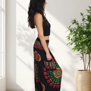 Puede incluir: Pantalones harem negros con un estampado floral colorido con detalles en rojo, amarillo y verde. Los pantalones se combinan con un top corto negro. El atuendo lo lleva una persona en una habitaci&oacute;n luminosa con una planta en maceta.