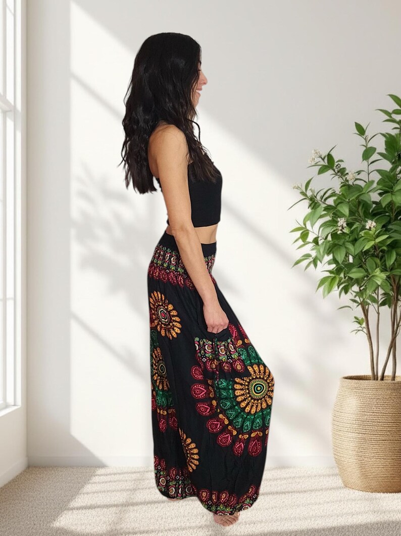 Puede incluir: Pantalones harem negros con un estampado floral colorido con detalles en rojo, amarillo y verde. Los pantalones se combinan con un top corto negro. El atuendo lo lleva una persona en una habitaci&oacute;n luminosa con una planta en maceta.