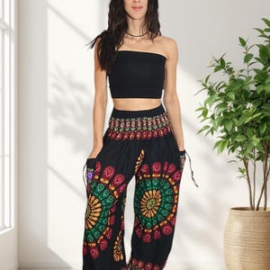 Puede incluir: Una mujer con un top de tubo negro y pantalones har&eacute;n negros. Los pantalones presentan un colorido dise&ntilde;o de mandala en tonos rojos, verdes, amarillos y morados. Los pantalones tienen bolsillos y detalles de cord&oacute;n.
