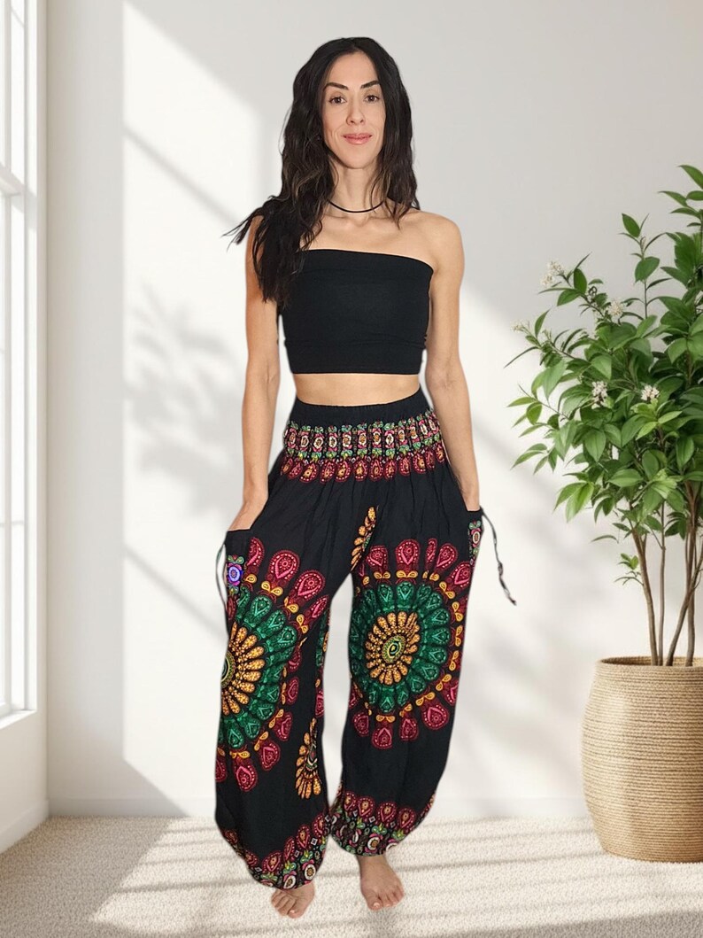 Puede incluir: Una mujer con un top de tubo negro y pantalones har&eacute;n negros. Los pantalones presentan un colorido dise&ntilde;o de mandala en tonos rojos, verdes, amarillos y morados. Los pantalones tienen bolsillos y detalles de cord&oacute;n.