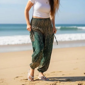 Puede incluir: Pantalones harén estampados en verde y marrón con cintura elástica. Los pantalones tienen un ajuste holgado y cómodo y se usan con un top corto blanco y chanclas en una playa de arena. Los pantalones presentan un diseño único y moteado.