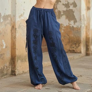 May include: Loose-fitting navy blue trousers featuring an elasticized waistband with a drawstring tie. The pants have side pockets and are decorated with vertical bands of black circular and geometric patterns running down the front of each leg.