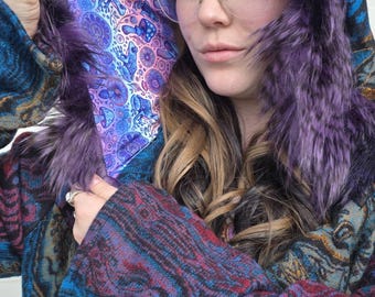 May include: A hooded coat with a vibrant, patterned design in shades of blue, purple, and brown. The hood is trimmed with purple faux fur, and the interior lining features a colorful, psychedelic print.