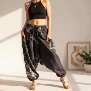 May include: Black harem pants with a white abstract design. The pants have pockets and a relaxed fit. The model is wearing a black halter top and white sandals. The pants are a comfortable and stylish choice for casual wear.