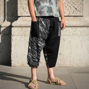 May include: Calf-length pants featuring a split design with one side in solid black and the other side in a black and white abstract marbled pattern. The pants include two large patch pockets on the front and a loose, relaxed fit silhouette.