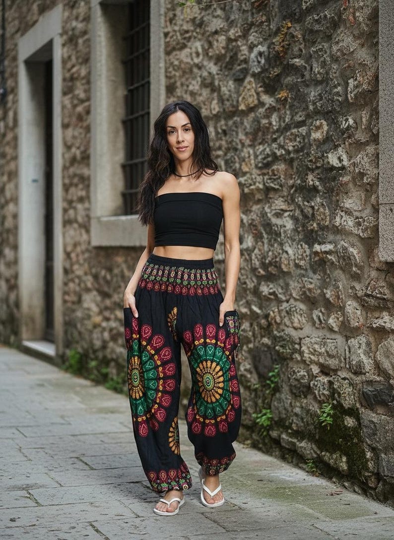 Puede incluir: Una persona con un top negro y pantalones harem negros con un dise&ntilde;o de mandala colorido. Los pantalones tienen bolsillos y se combinan con sandalias blancas. El fondo es una pared de piedra y un camino pavimentado.