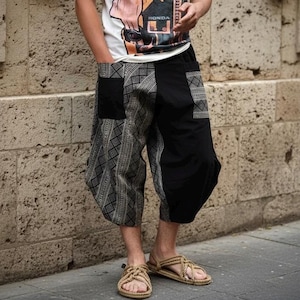 May include: Cropped pants featuring a split design with one side in solid black and the other side in a grey and black geometric diamond pattern. The pants include two large patch pockets with matching geometric trim and a loose, wide-leg fit.