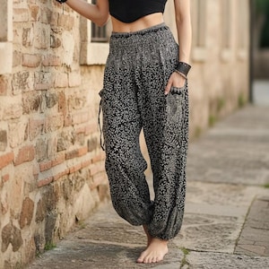 May include: Black and white patterned harem trousers with pockets. The trousers have a loose fit and a drawstring waist. The fabric features a repeating floral design.