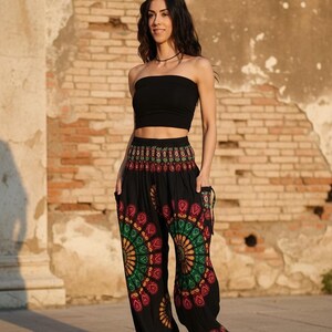 Puede incluir: Una mujer con un top de tubo negro y pantalones harem negros con un colorido dise&ntilde;o de mandala. Los pantalones tienen bolsillos y se combinan con sandalias blancas. El fondo es una pared de ladrillo desgastada.